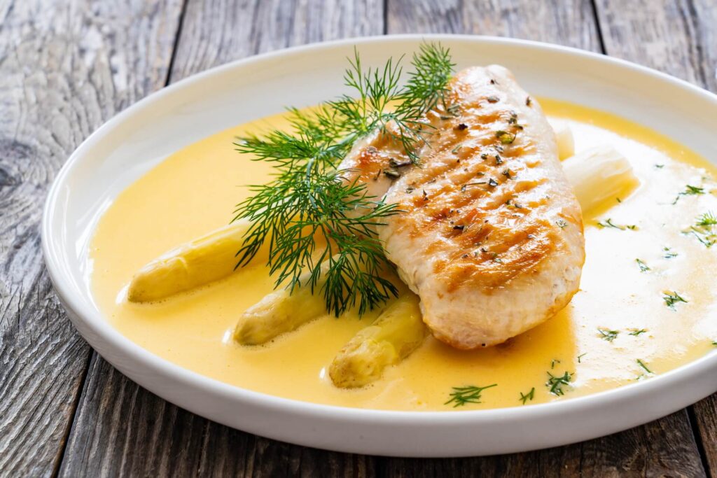 elingea-recipe Grilled chicken breast and white asparagus in hollandaise sauce on wooden table